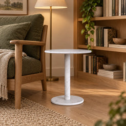 RoundHaven Carrara marble Standard side table beside an oak reading chair, shown from a low front-quarter view
