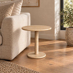 RoundHaven Classico travertine side table with a round top and circular base beside a linen sofa.
