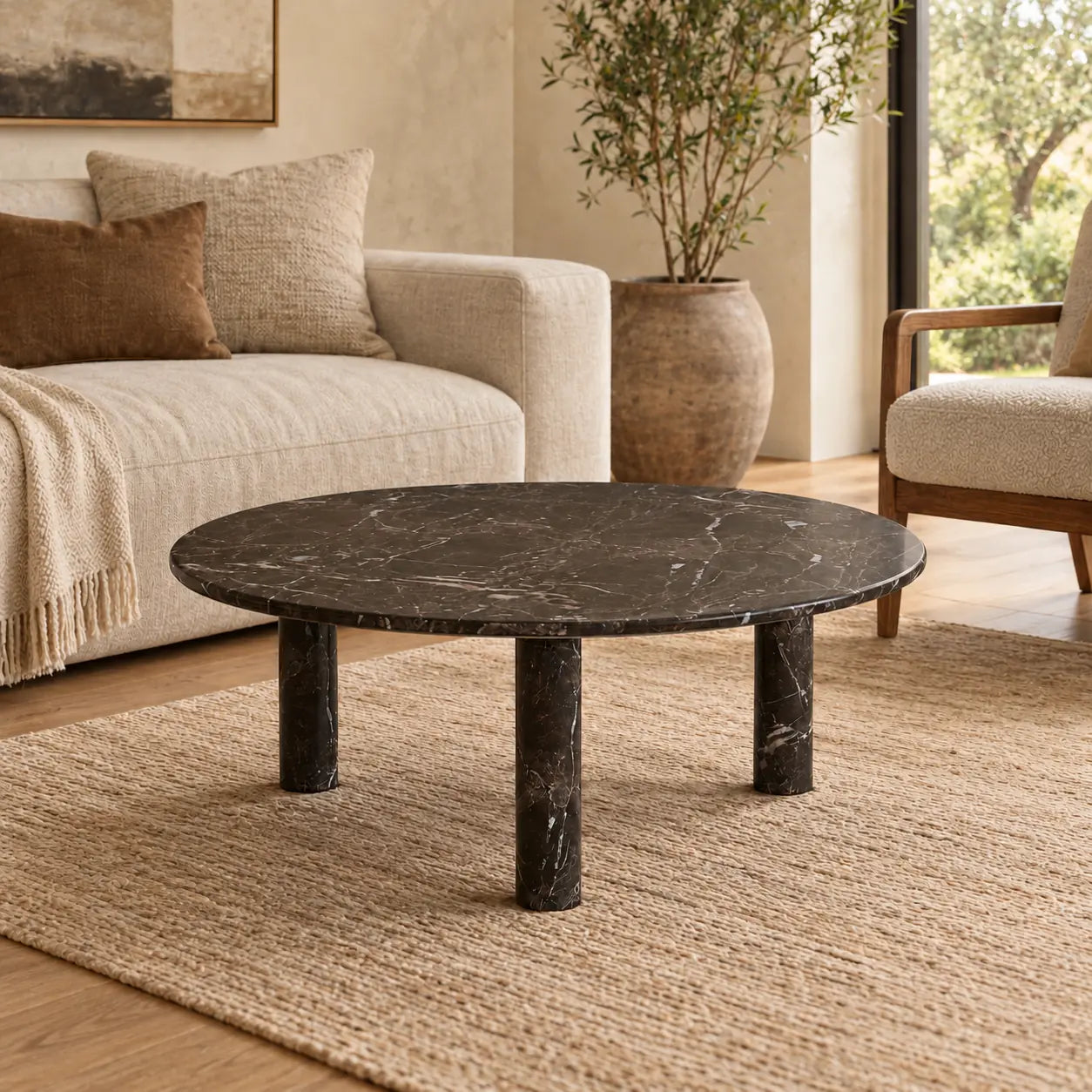 RoundHaven Spanish Dark Emperador marble coffee table with a thin circular top and three cylindrical legs in a warm oatmeal-sofa living room.