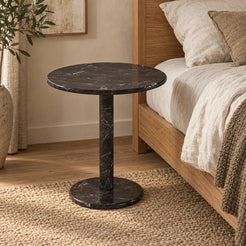 Moderate view of the RoundHaven Dark Emperador marble side table beside a linen bed.
