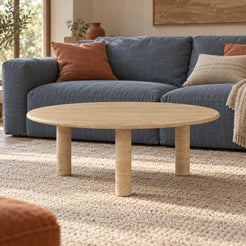 Low view of the RoundHaven travertine coffee table in a relaxed TV lounge, showing its thin round top and three stone legs.