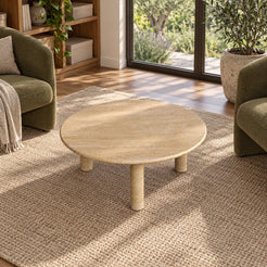 Elevated view of the RoundHaven travertine coffee table in a garden-facing reading room, with the circular top and three-legged form visible.