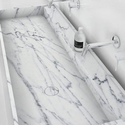 Close view of the Tahira Carrara marble trough basin showing natural veining and a drain