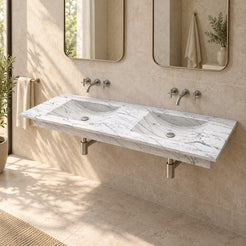 Taiya Carrara White Marble Wall-Mounted Sink in a warm stone bathroom, showing its complete double basin, sloping carved wash areas and floating profile