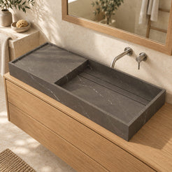 Tavira Integrated Perlato Marble Basin in a warm limestone and oak bathroom, viewed from above with the left stone surface, right wash basin and linear drainage detail visible