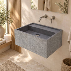 Tibna Wall-Mounted Neroco Stone Sink in a warm ivory and oak bathroom, viewed from the front left with the complete basin and chiseled stone exterior visible