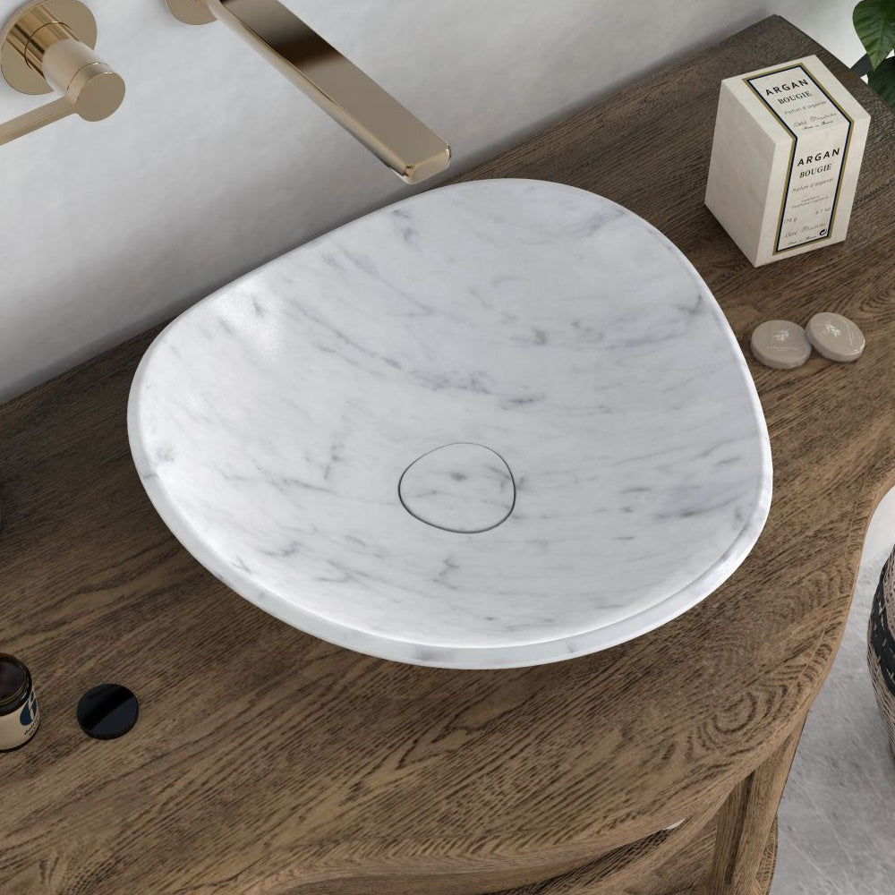 Sita Carrara marble specialty vessel sink with a rounded triangular bowl, overhead angle on a wooden vanity