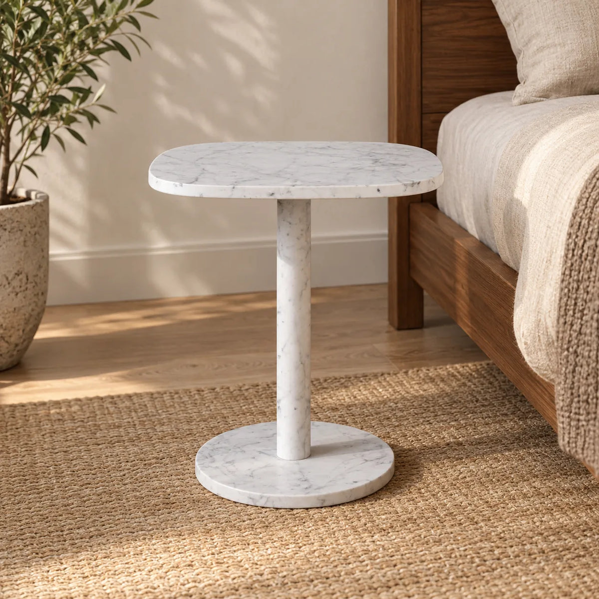 SquareSoft Carrara marble side table shown from a low angle beside a walnut bed.