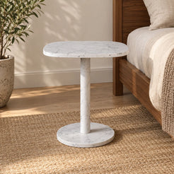 SquareSoft Carrara marble side table shown from a low angle beside a walnut bed.