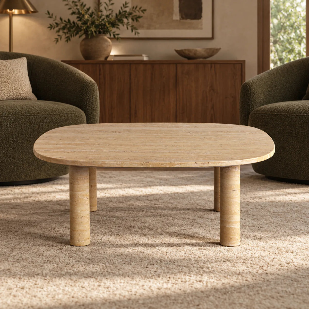 Low front view of the SquareSoft travertine coffee table in a relaxed den, showing the thin rounded-square top and stone legs.