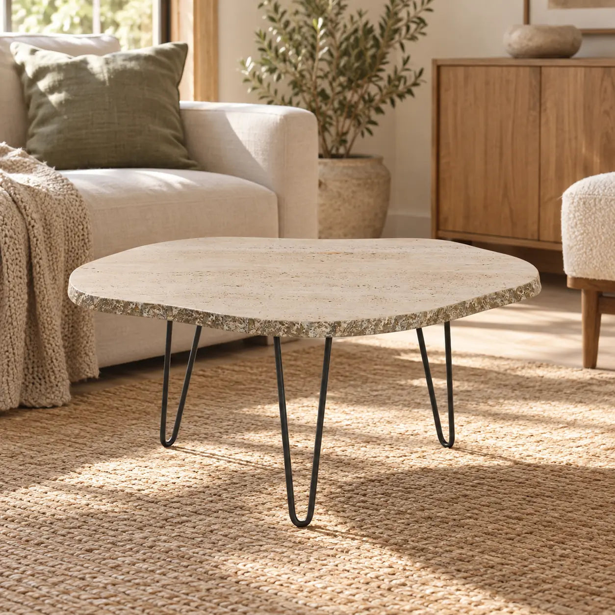 StoneMist travertine coffee table with an irregular top and black hairpin legs in a sunlit living corner.