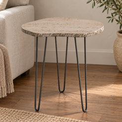 StoneMist travertine side table on three dark hairpin supports beside a linen sofa, shown from a mid-height front view
