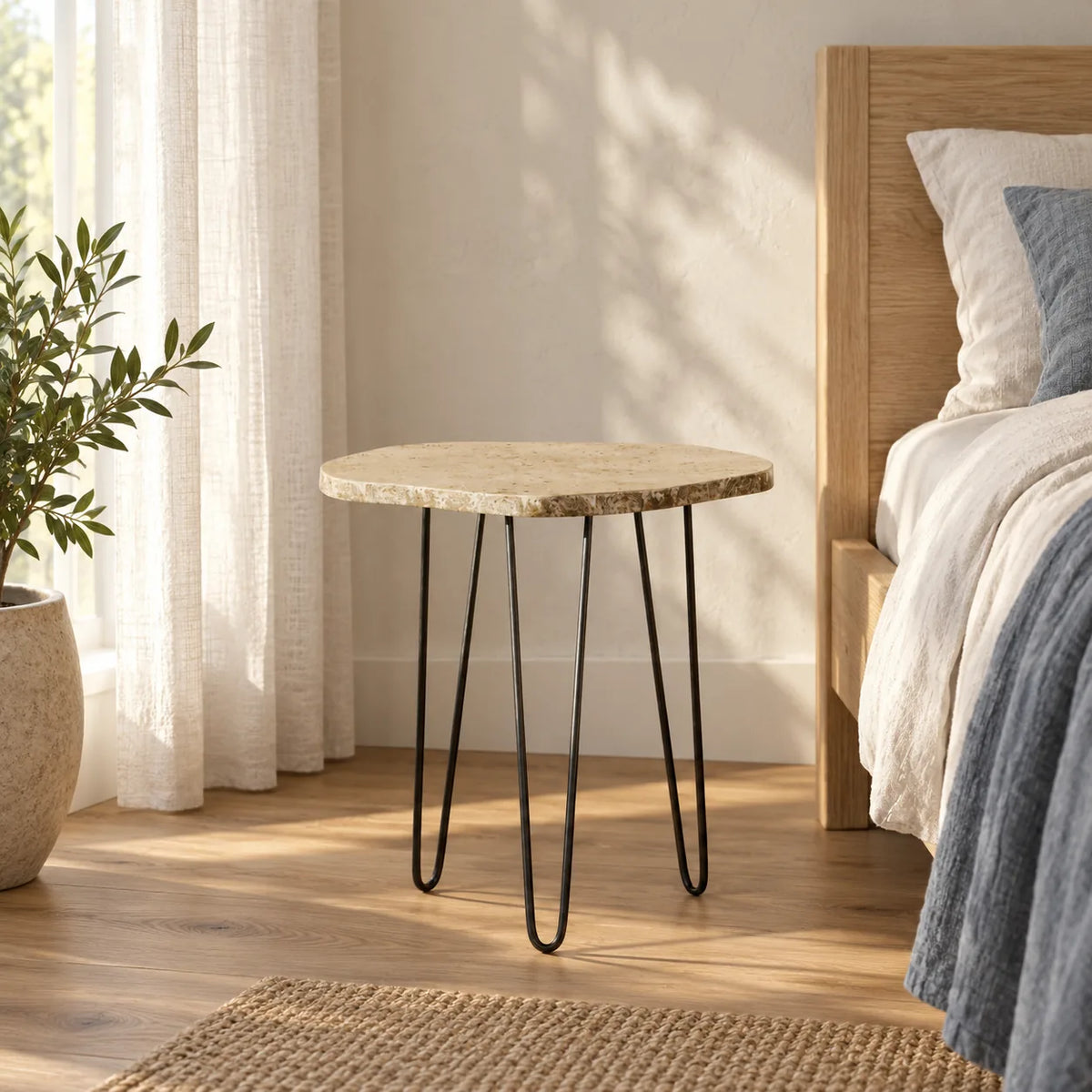 StoneMist travertine side table beside a linen bed, shown from a low front-quarter view with three hairpin supports