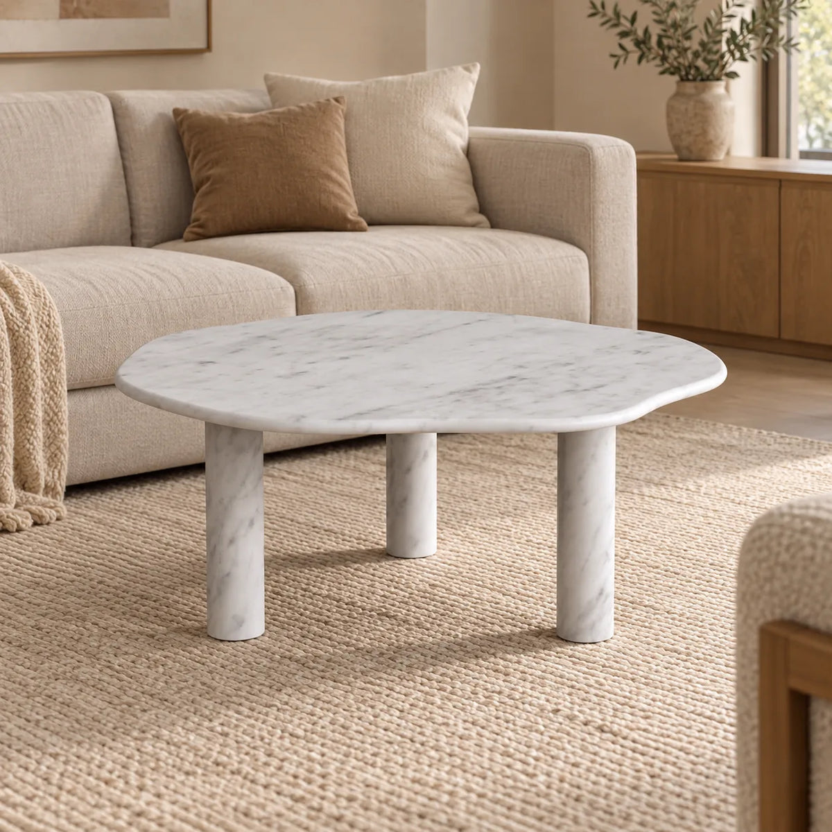 SunAura Carrara marble coffee table with a softly lobed top and three cylindrical legs in a warm living room.
