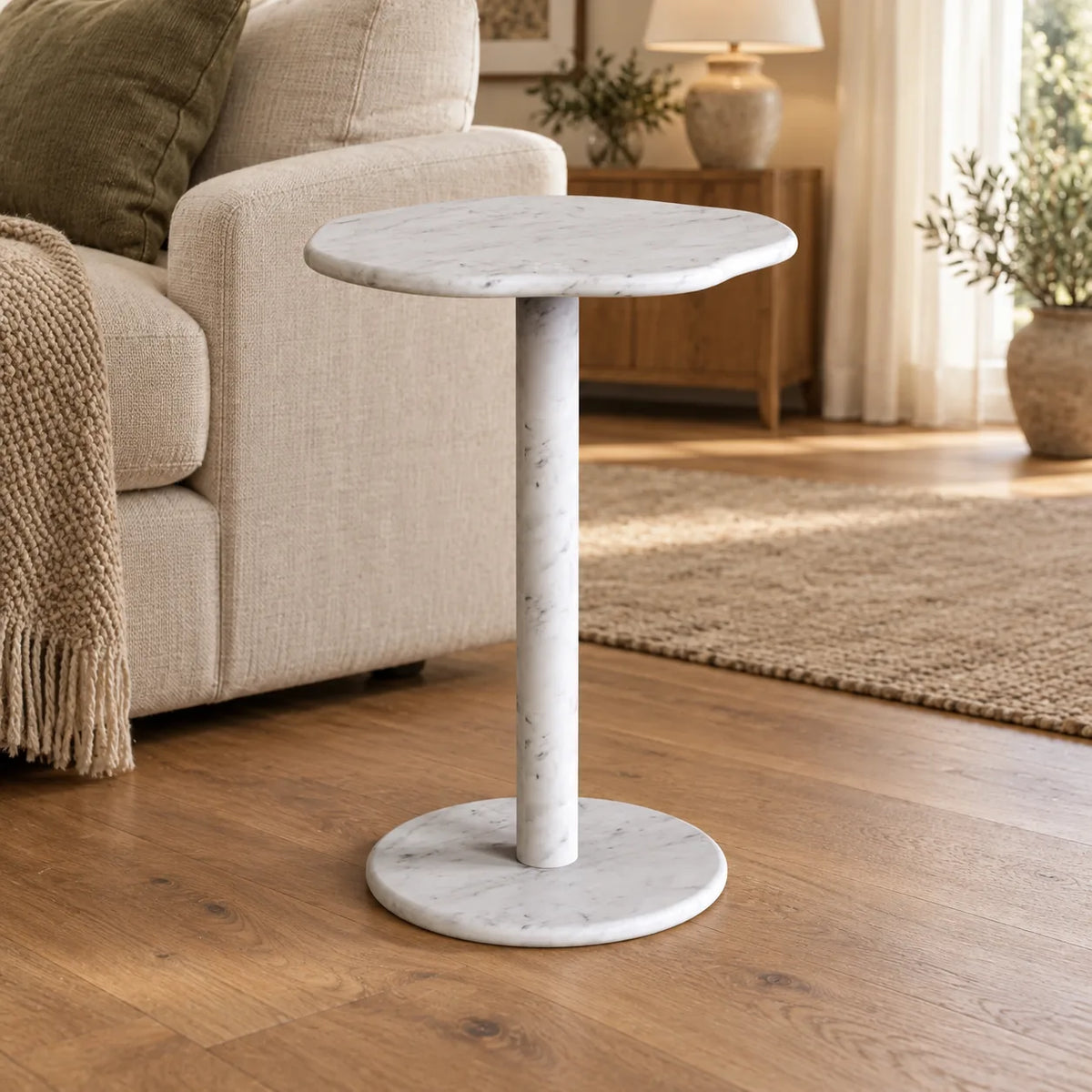 SunAura Carrara marble side table beside a linen sofa, shown from a moderately elevated front view