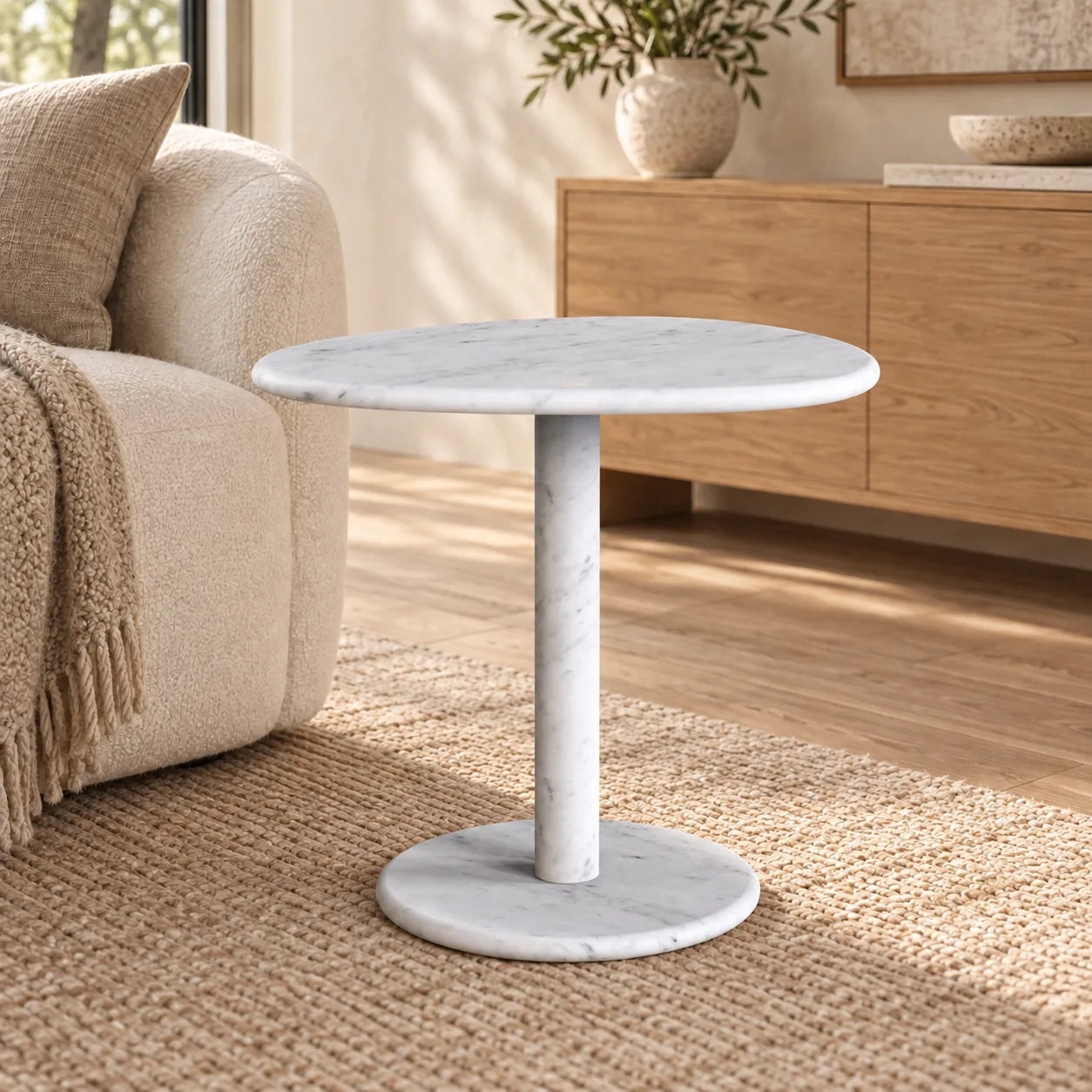 SwanEgg Carrara marble side table with an oval top and circular base beside an off-white sofa.
