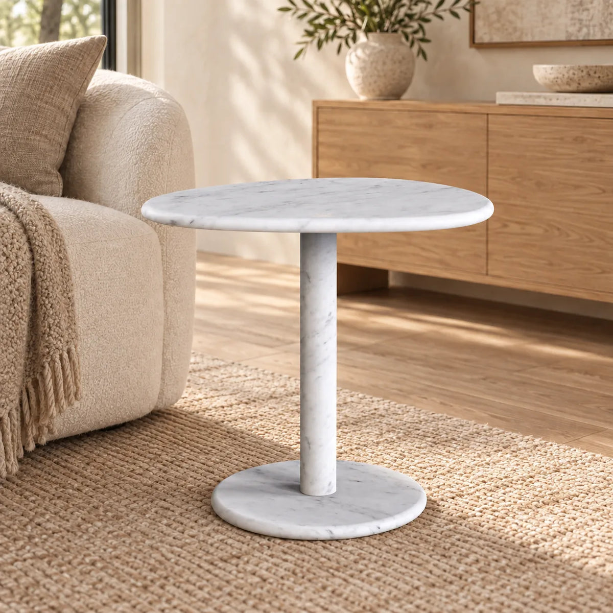 SwanEgg Carrara marble side table with an oval top and circular base beside an off-white sofa.