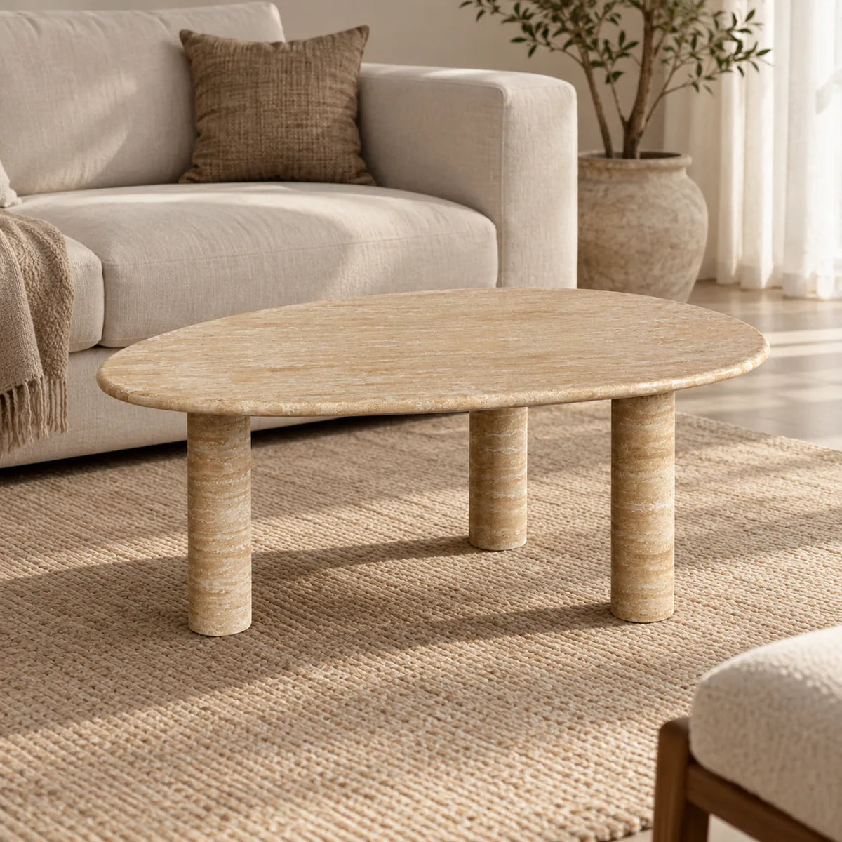 SwanEgg Italian Classico travertine coffee table with a thin oval top and three cylindrical legs in a warm linen-sofa living room.