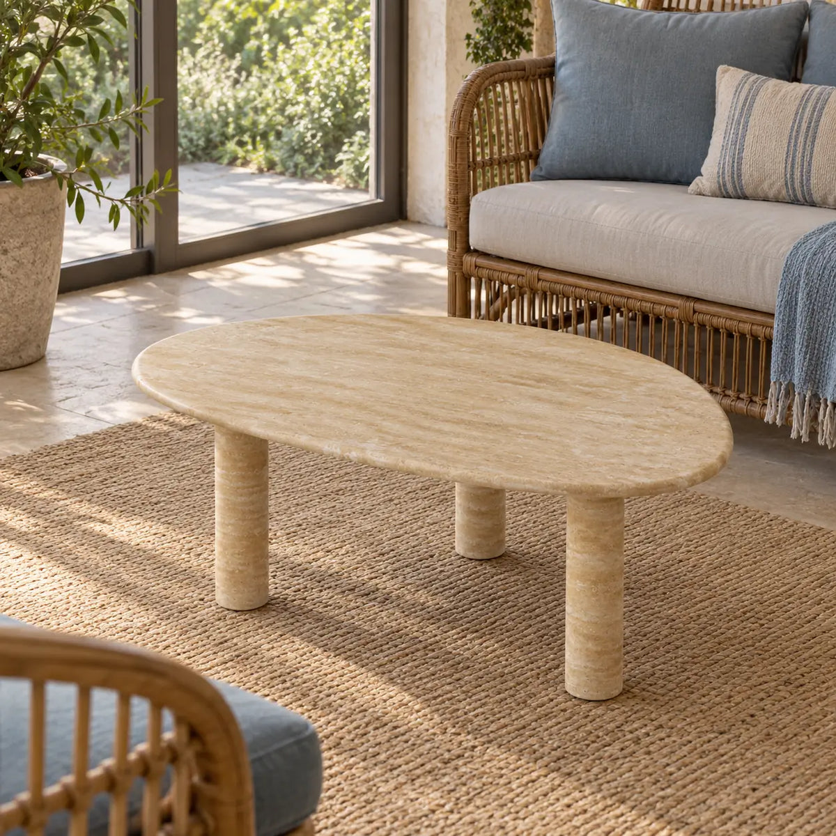 Elevated view of the SwanEgg Classico travertine coffee table in a garden-facing sunroom, showing its oval stone top and three cylindrical legs.