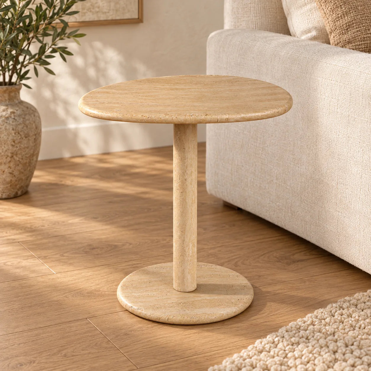 SwanEgg Classico travertine side table with an oval top and circular base beside a linen sofa.