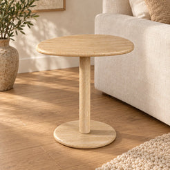 SwanEgg Classico travertine side table with an oval top and circular base beside a linen sofa.