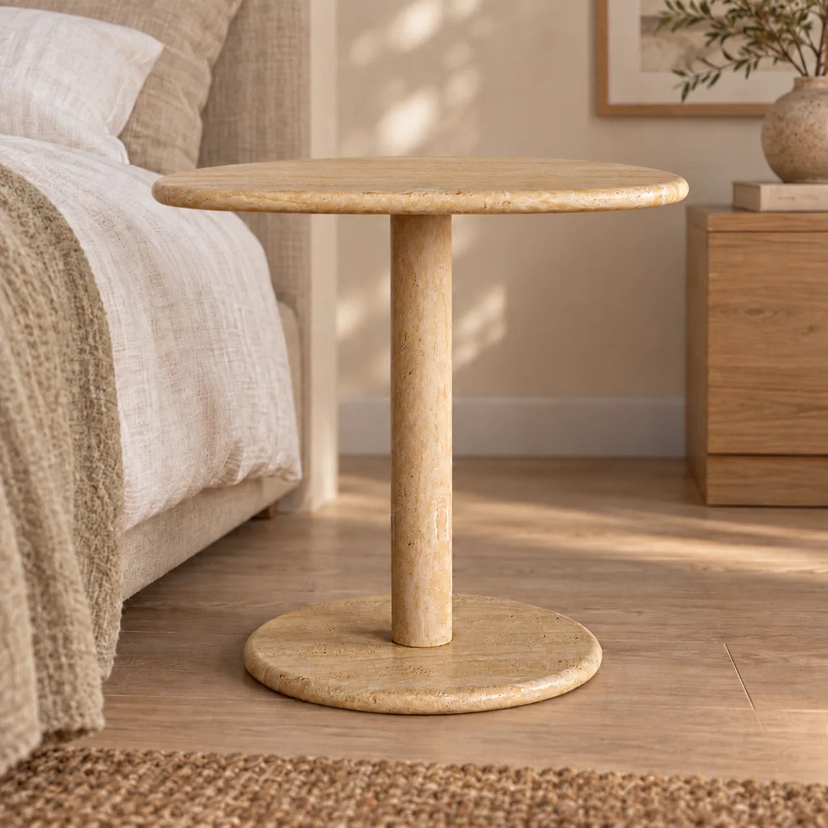 Low frontal view of the SwanEgg travertine side table beside a timber bed.