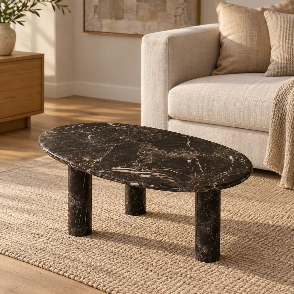 SwanEgg Spanish Dark Emperador marble coffee table with a thin oval top and three cylindrical legs in a warm linen-sofa living room.