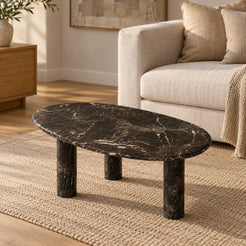 SwanEgg Spanish Dark Emperador marble coffee table with a thin oval top and three cylindrical legs in a warm linen-sofa living room.