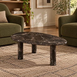Low front view of the SwanEgg Dark Emperador marble coffee table in a green-chair reading lounge, showing its thin egg-shaped top and three stone supports.