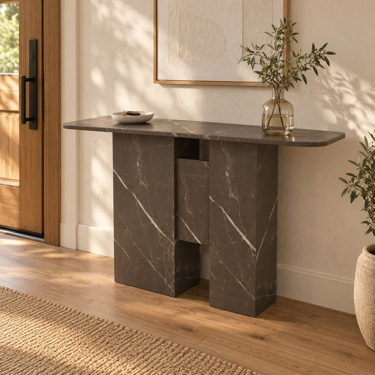 Right-front view of the Thalia Bulgarian Gray marble console in a warm entryway, showing its thin rounded-end top and two stone supports with a raised central panel
