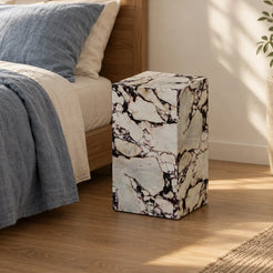 ViolaPlinth Calacatta Viola marble side table beside a linen bed, shown from a moderately elevated front-quarter view