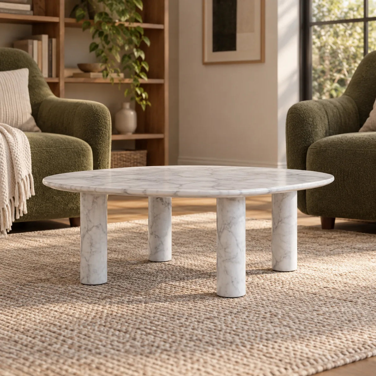 Low front view of the ZenPebble Carrara marble coffee table in a green-chair reading lounge, showing its rounded-square top and four stone supports.