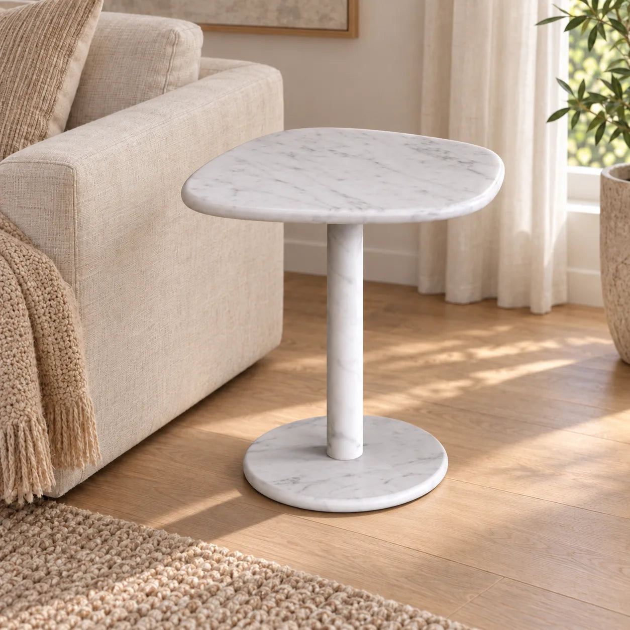 ZenPebble Italian Carrara marble side table with a pebble-shaped top beside a linen sofa, shown from a moderate oblique view
