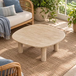 Elevated view of the ZenPebble Classico travertine coffee table in a garden-facing sunroom, showing its soft-square stone top and four cylindrical legs.