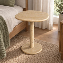 Moderate view of the ZenPebble travertine side table beside a timber bed.