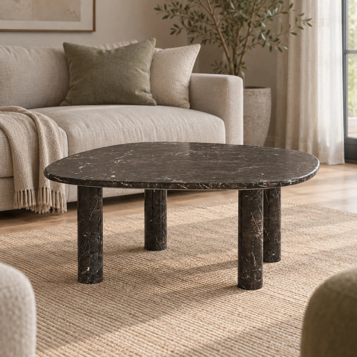 Low front view of the ZenPebble Dark Emperador marble coffee table in a linen-sofa living room, showing its thin rounded-square top and four stone legs.