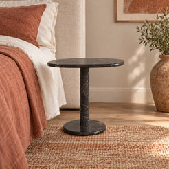 ZenPebble Dark Emperador marble side table beside a bed, shown from a low frontal view