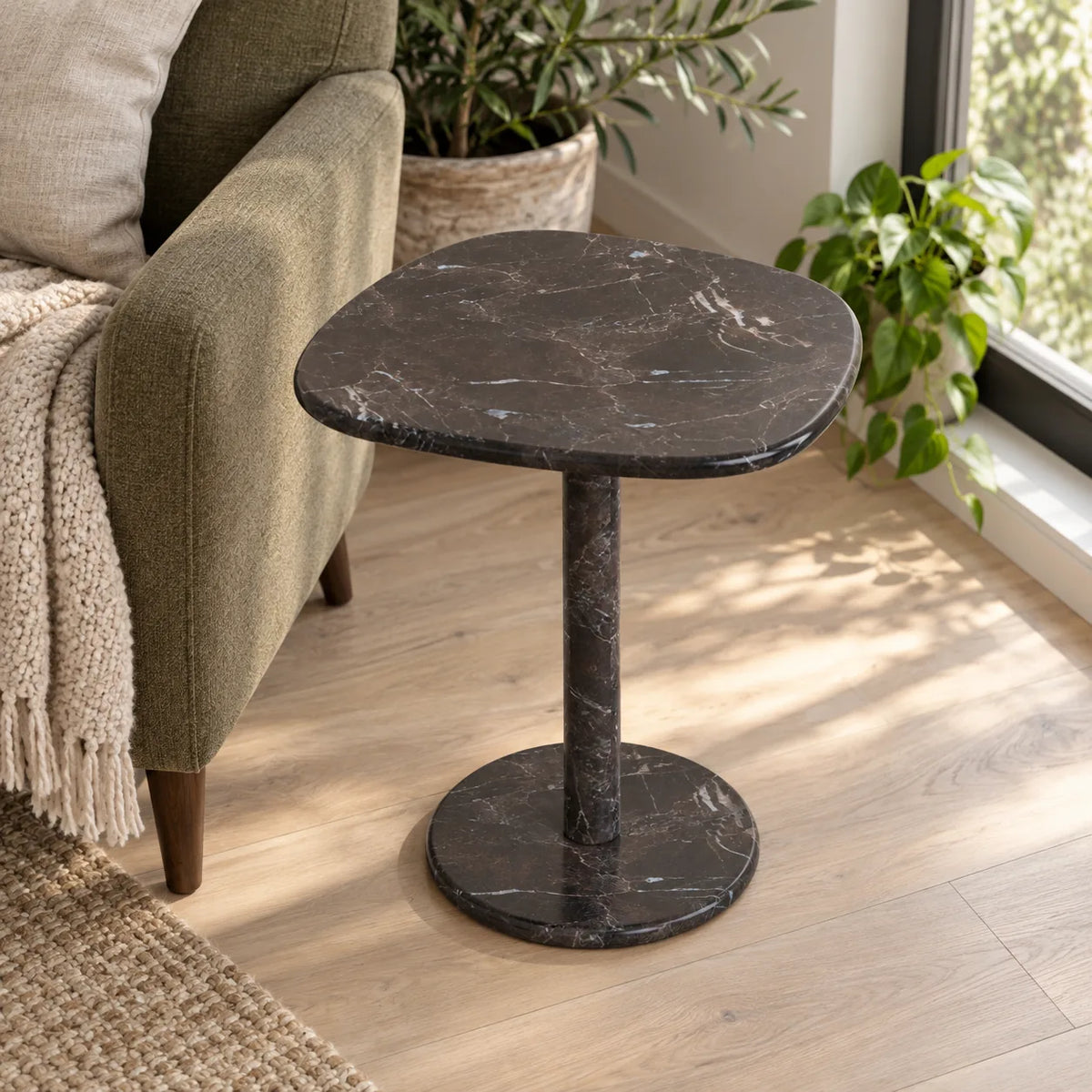 ZenPebble Dark Emperador marble side table in a window reading corner, shown from an elevated oblique view